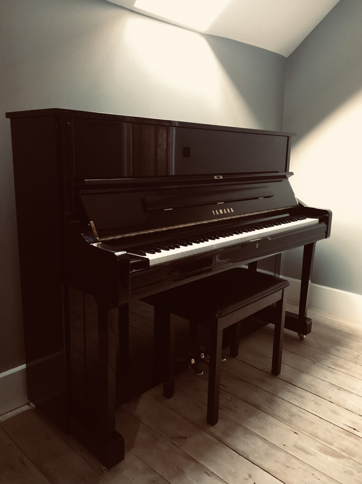 Polished ebony Yamaha and stool stood against a grey wall.