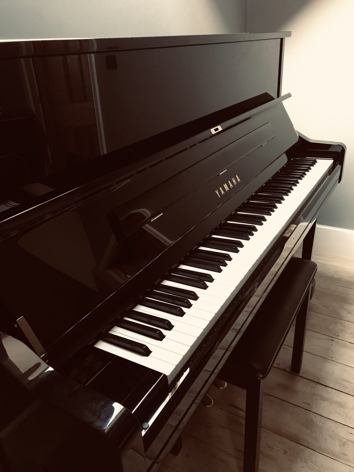 Close up of polished ebony Yamaha and stool stood against a grey wall.