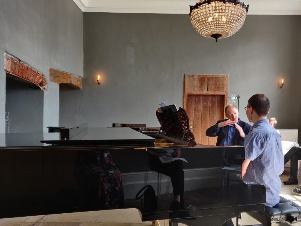 Warren Mailley-Smith instructing a student, both sat at their own grand piano