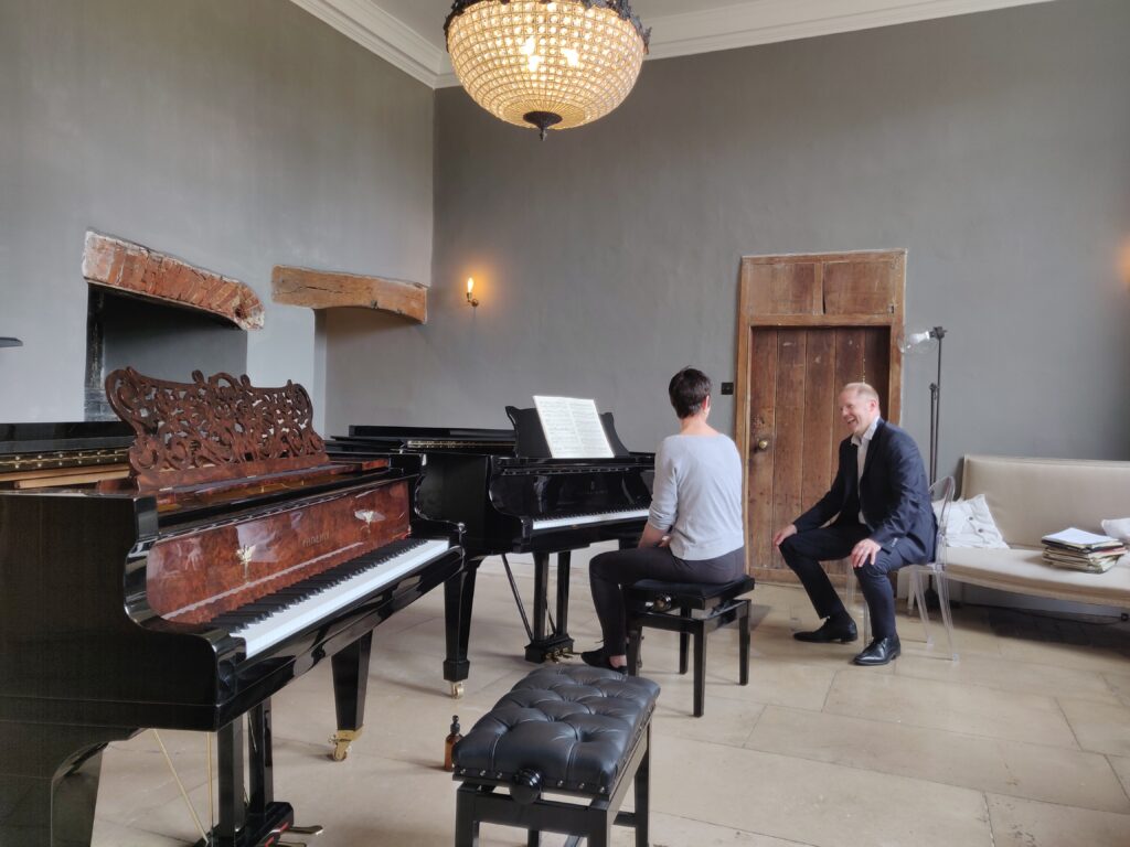 Warren laughing with student who is sat at the Steinway in the recital room. There is another grandpiano in the foreground.