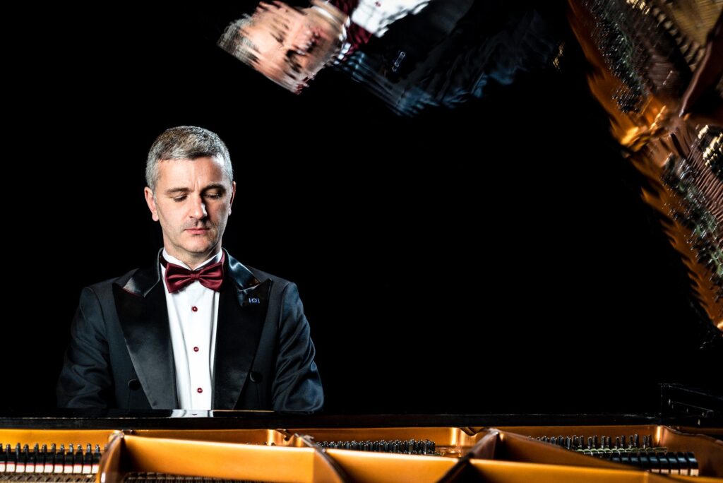 Daniel Grimwood playing at grand piano with reflection in the lid