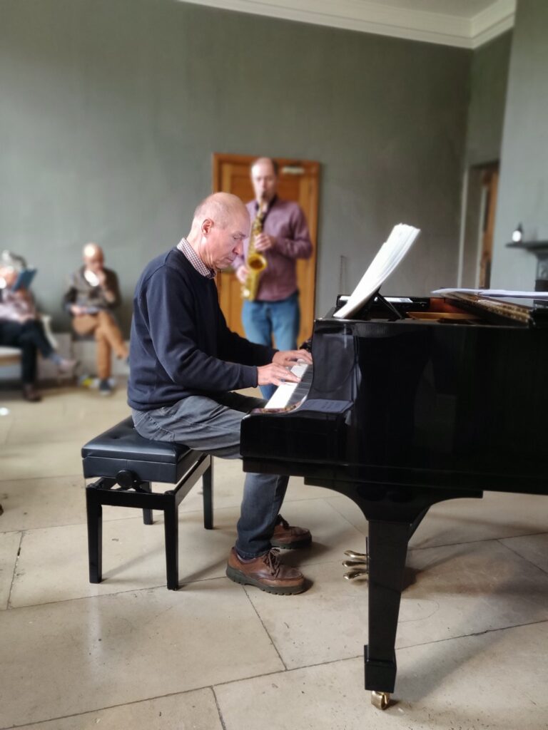Man playing grand piano with saxophonist in background