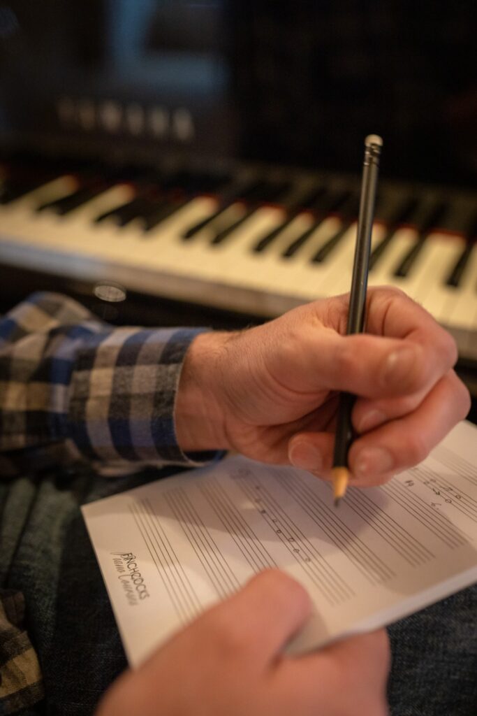 Close up of man writing on manuscript paper, sat at a Yamaha grand piano