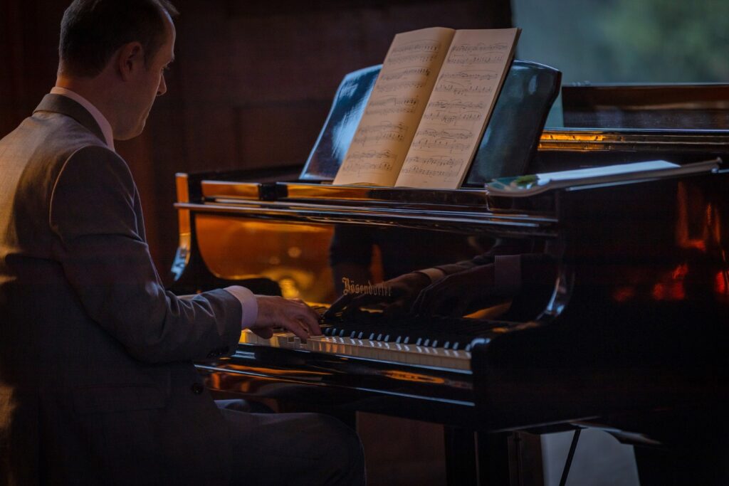 man in suit playing grand piano with firelight reflecting on it