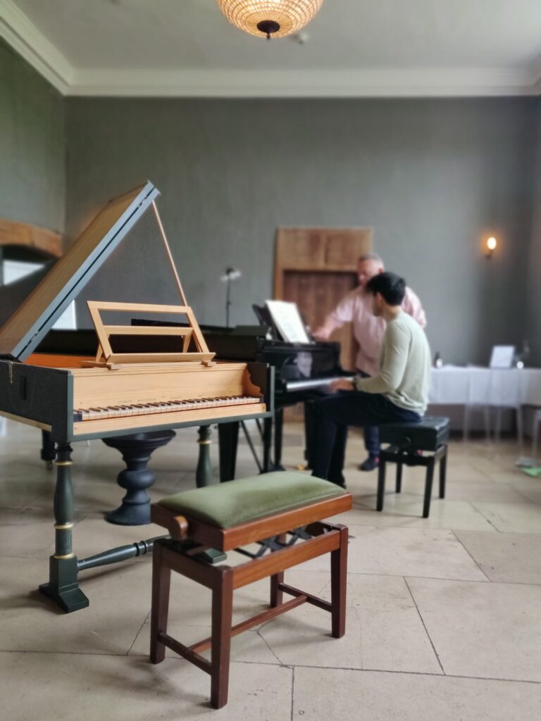 Harpsichord in foreground with student and teacher in background on Steinway piano