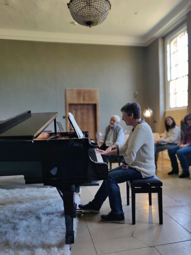 Performance class in the recital room with Jenny smiling at the Steinway in the foreground and William Westney smiling in the background