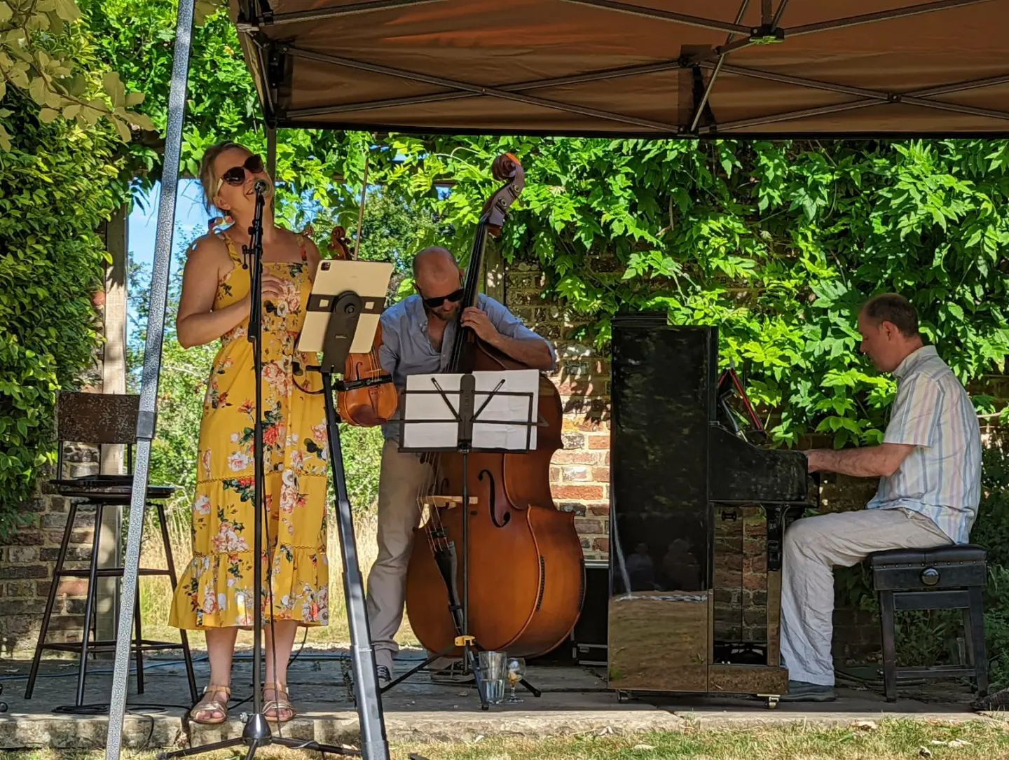Jazz trio comprising of vocalist, double bass and piano under a gazebo.
