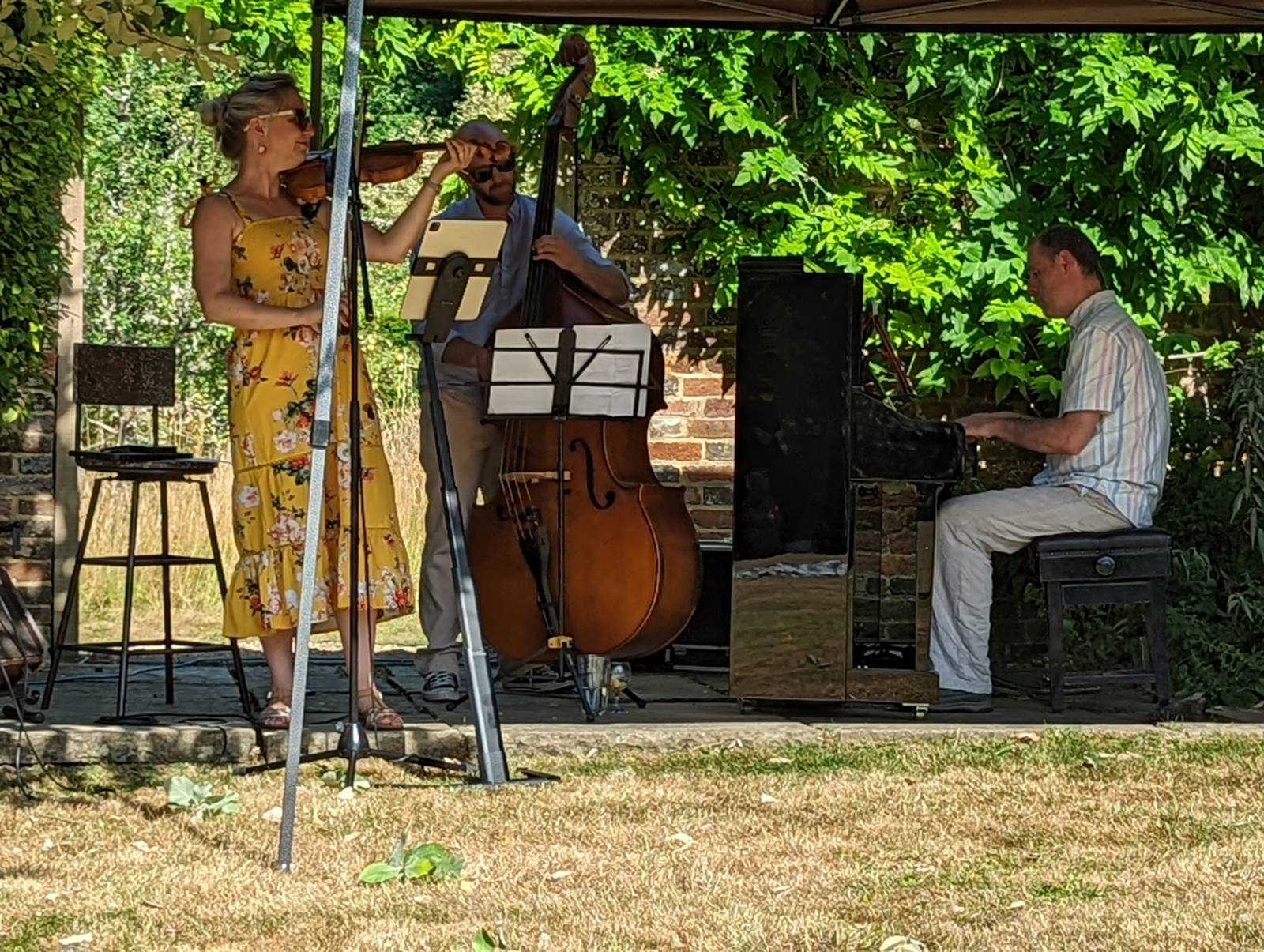 Jazz trio comprising of violinist, double bass and piano under a gazebo.