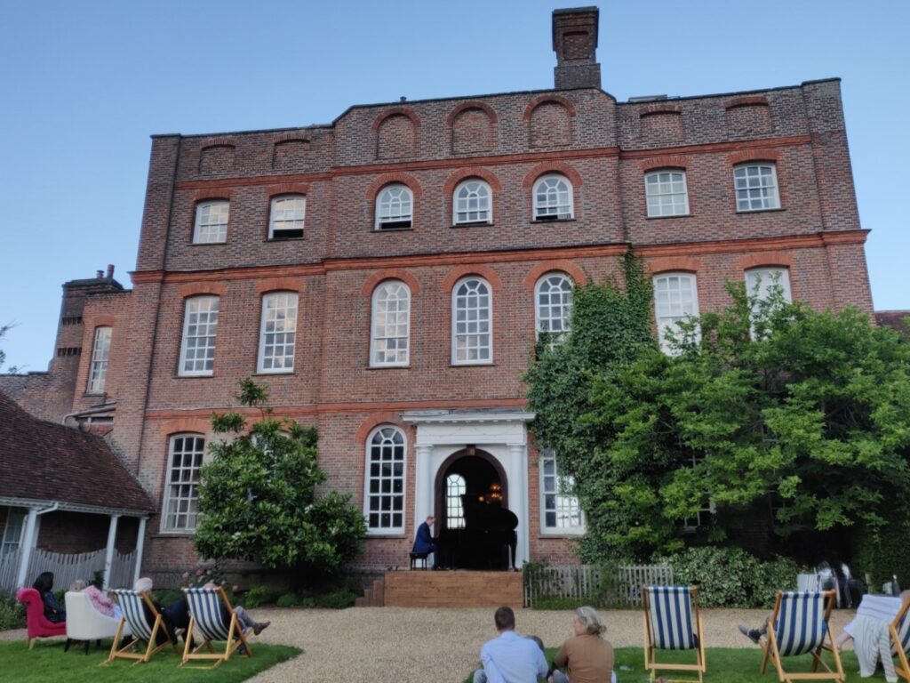 West elevation of Finchcocks with Warren Mailley-Smith performing on open-air stage to course guests on the lawn.